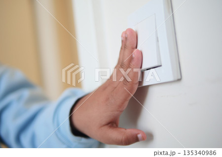 A child hand is pressing a light switch on a wall inside a room A child hand is pressing a light switch on a wall inside a room 135340986
