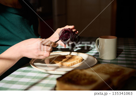 Morning Toast With Jam: Person Spreading Berry Jam On Toast At Breakfast Table Morning Toast With Jam: Person Spreading Berry Jam On Toast At Breakfast Table 135341063