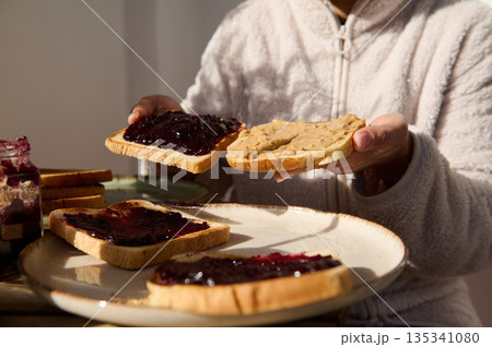 Person Spreading Peanut Butter and Jelly on Toasts for Breakfast Joy 135341080