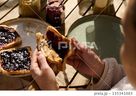 Family Breakfast Outdoors Spreading Peanut Butter and Jam on Toast at a Rustic Picnic Table 135341083