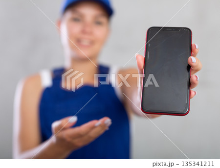 Young woman in work overalls posing with phone Young woman in work overalls posing with phone 135341211