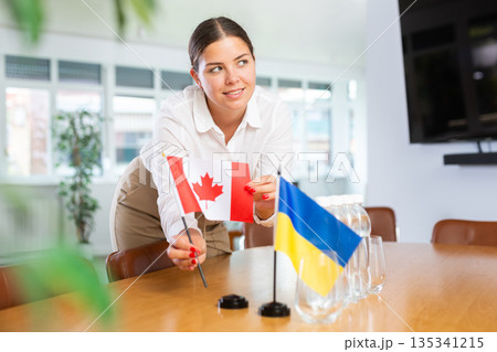 Young lady sets miniatures flags of Ukraine and Canada for international negotiations 135341215