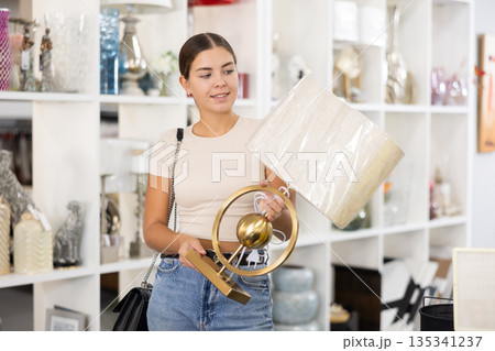 Smiling female purchaser choosing stylish table lamp in shop 135341237