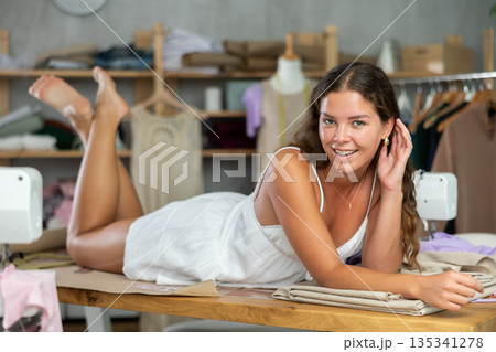 Female dressmaker lying playfully on table in workshop Female dressmaker lying playfully on table in workshop 135341278