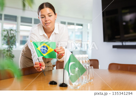 Positive young woman putting little flag of Brazil on table next to the flag of Pakistan 135341294