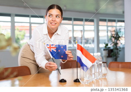 Young woman puts New Zealand and Netherlands flags on table in office 135341368