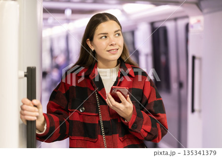 Girl is standing with phone in subway car, getting to work Girl is standing with phone in subway car, getting to work 135341379