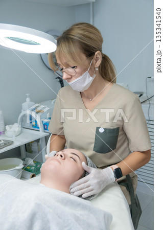 Cosmetologist Facial Treatment Skincare Clinic: Professional performs facial treatment in modern beauty clinic. Cosmetologist Facial Treatment Skincare Clinic: Professional performs facial treatment in modern beauty clinic. 135341540