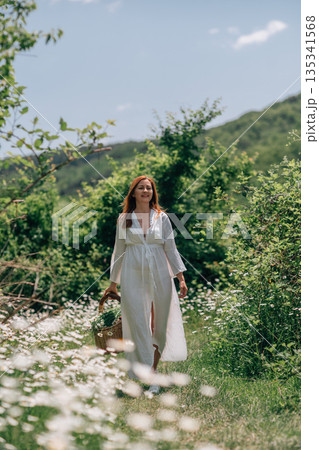 Woman Basket Daisies: Summer day; red-haired woman carries flower basket in chamomile field for foraging. Woman Basket Daisies: Summer day; red-haired woman carries flower basket in chamomile field for foraging. 135341568