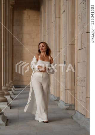 Woman White Outfit Architecture - A woman in an all-white outfit stands in front of a classic architecture building. 135341583
