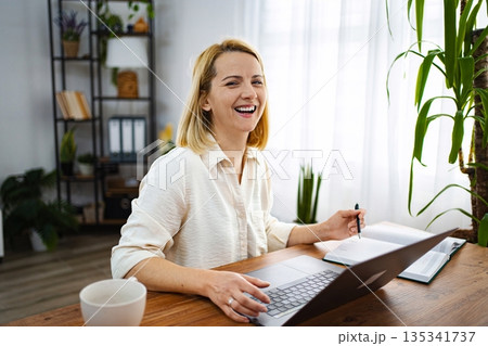 Smiling woman working on laptop in bright home office 135341737