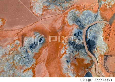 Geothermal area in Iceland with vibrant orange and blue hues, bubbling mud pots, steaming vents, rugged terrain, and a wooden boardwalk for visitors. Geothermal area in Iceland with vibrant orange and blue hues, bubbling mud pots, steaming vents, rugged terrain, and a wooden boardwalk for visitors. 135343354