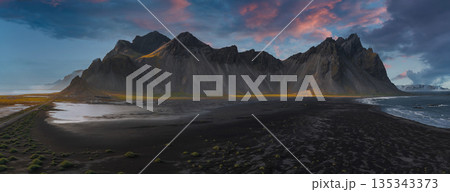 The Stokksnes Peninsula features Vestrahorn's jagged peaks, a black sand beach, gentle waves, green moss, and a colorful sunset sky. 135343373