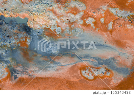 Vibrant orange and rust colored earth with gray and white deposits, bubbling mud pots, and steaming vents highlight Iceland's geothermal activity. 135343458
