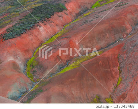 The Rainbow Mountains in Iceland display red, orange, and green hues, with moss and vegetation contrasting against the mineral rich terrain. The Rainbow Mountains in Iceland display red, orange, and green hues, with moss and vegetation contrasting against the mineral rich terrain. 135343469