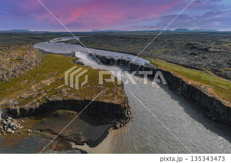 Studlagil Canyon in Iceland features basalt columns, a winding river, and vibrant moss under a pink and purple sky during sunset or sunrise. Studlagil Canyon in Iceland features basalt columns, a winding river, and vibrant moss under a pink and purple sky during sunset or sunrise. 135343473