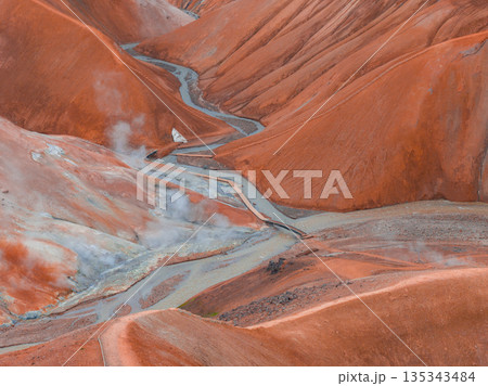 Rust colored rhyolite hills with steam vents, a winding stream, and wooden walkways in the Kerlingarfjoll geothermal area of Iceland. 135343484