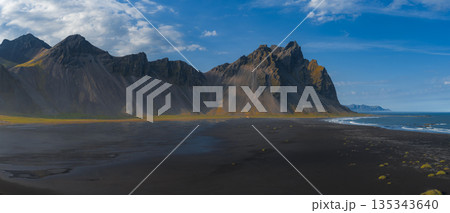 The Stokksnes Peninsula in Iceland features the jagged Vestrahorn mountain, a black sand beach, green vegetation, and waves from the North Atlantic Ocean. The Stokksnes Peninsula in Iceland features the jagged Vestrahorn mountain, a black sand beach, green vegetation, and waves from the North Atlantic Ocean. 135343640