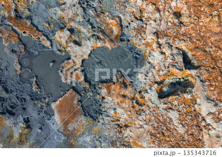 Aerial image of an Icelandic geothermal area featuring bubbling mud pots, grayish blue pools, and orange brown terrain with vibrant mineral deposits. 135343716