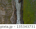 Aerial perspective of a steep canyon in Iceland, featuring a milky river cutting through rugged terrain on one side and green vegetation on the other. 135343731
