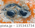 Aerial image of two bubbling mud pots surrounded by orange and white mineral deposits, showcasing geothermal activity in Iceland's volcanic terrain. 135343734