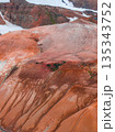 Aerial view of Iceland's Rainbow Mountains, featuring vibrant red, orange, and brown rhyolite formations with contrasting snow patches in the background. 135343752
