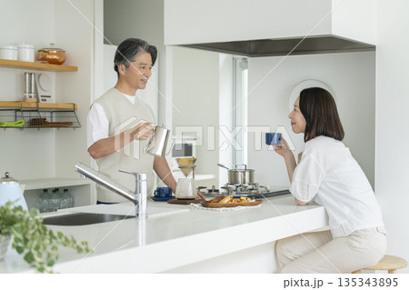 50代の夫婦　イメージ　キッチンでコーヒー淹れる男性とコーヒーを飲む女性 135343895