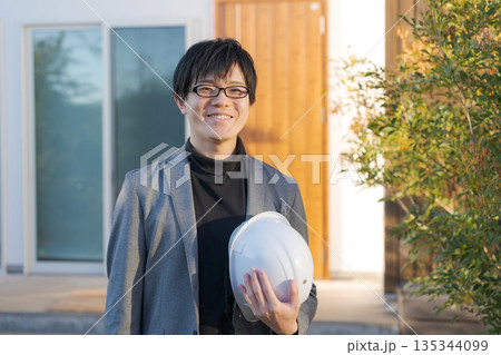 一軒家の前に立つヘルメットを持った男性 135344099