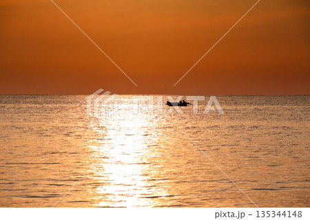 Silhouette of a small boat on the sea at sunset with golden light reflecting on the water, creating a peaceful seascape, and copy space for inspirational travel quotes 135344148