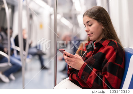 girl sitting in subway car with phone girl sitting in subway car with phone 135345530