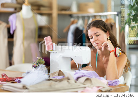 Sad dressmaker sitting at sewing machine in studio Sad dressmaker sitting at sewing machine in studio 135345560