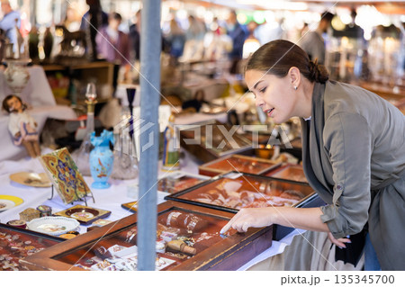 Cheerful female tourist choosing antique jewelry at flea market 135345700