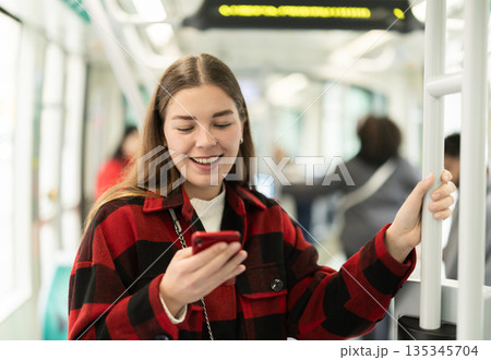 Girl is standing with phone in tram car, getting to work 135345704