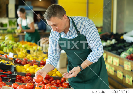 Portrait of man in apron selling organic tomatoes in grocery shop 135345750