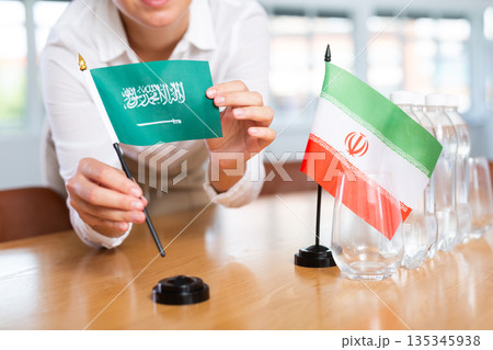 Little flag of Iran on table and flag of Saudi Arabia put next to it by young woman 135345938