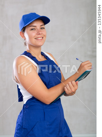 Happy female worker in work clothes making notes in file with papers Happy female worker in work clothes making notes in file with papers 135345944