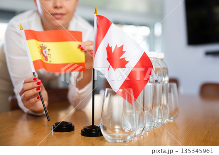 Young woman putting flags of Spain and Canada on table in office 135345961