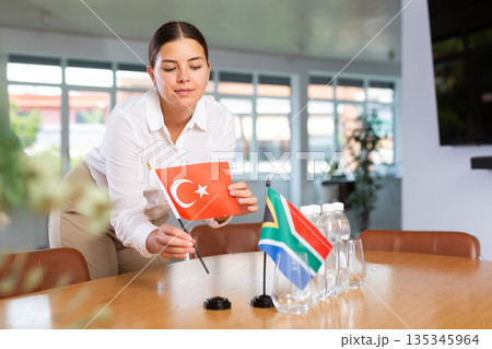 Positive young woman putting little flag of Turkey on table next to the flag of South Africa Positive young woman putting little flag of Turkey on table next to the flag of South Africa 135345964