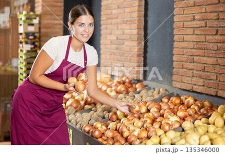 Girl seller working in supermarket and lays out onions on counter 135346000