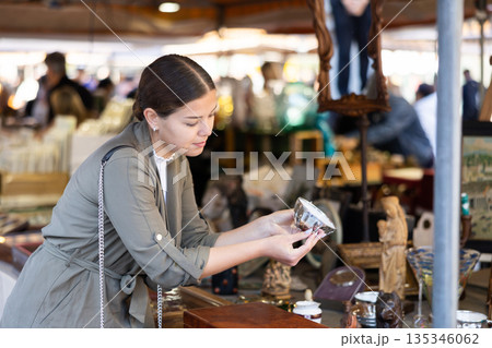 Young woman looking at antique cup at flea market 135346062