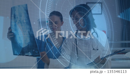 Two medics in scrubs holding X-ray film and reviewing clipboard in exam room with digital overlay 135346113