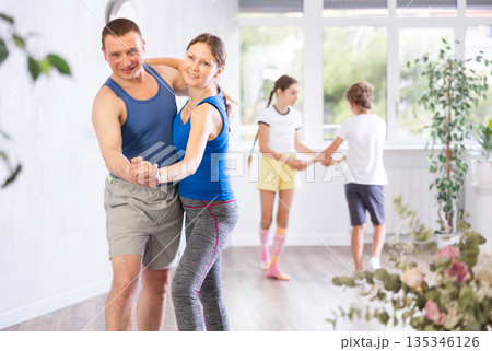 Joyful middle-aged parents practicing dance in pairs against their children holding hands while training together in wellness studio 135346126