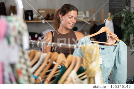 Girl customer choose dress in store, and buyer carefully examines product. Girl customer choose dress in store, and buyer carefully examines product. 135346149