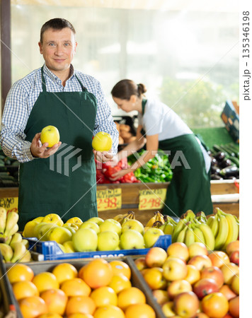 Man seller working in supermarket and lays out apples on counter Man seller working in supermarket and lays out apples on counter 135346198