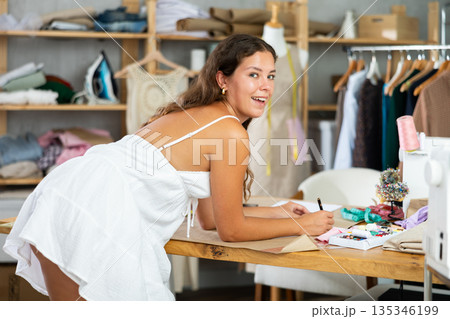 Dressmaker draws a model of clothes on paper in a workshop 135346199