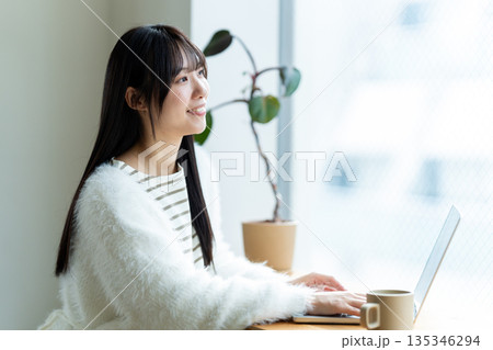 窓際でノートパソコンを操作する笑顔の女性 135346294