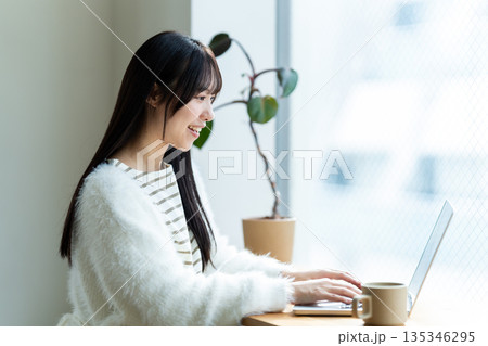 窓際でノートパソコンを操作する笑顔の女性 窓際でノートパソコンを操作する笑顔の女性 135346295