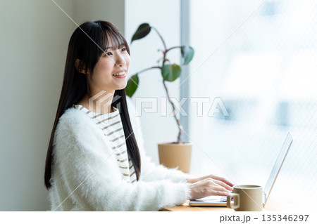 窓際でノートパソコンを操作する笑顔の女性 135346297