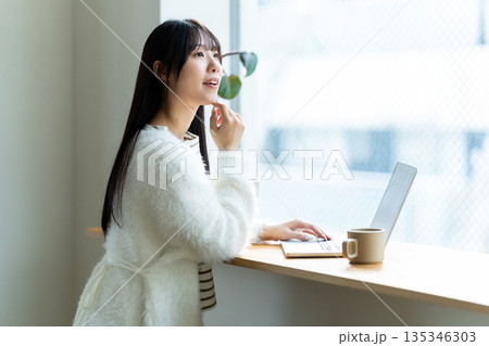 窓際でノートパソコンを操作する笑顔の女性 窓際でノートパソコンを操作する笑顔の女性 135346303