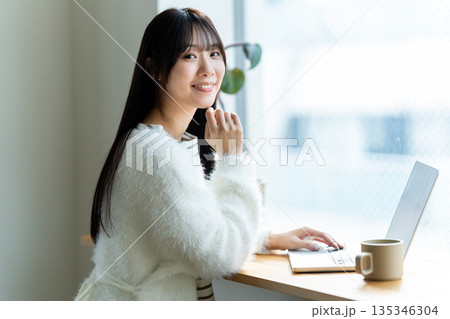 窓際でノートパソコンを操作する笑顔の女性 135346304